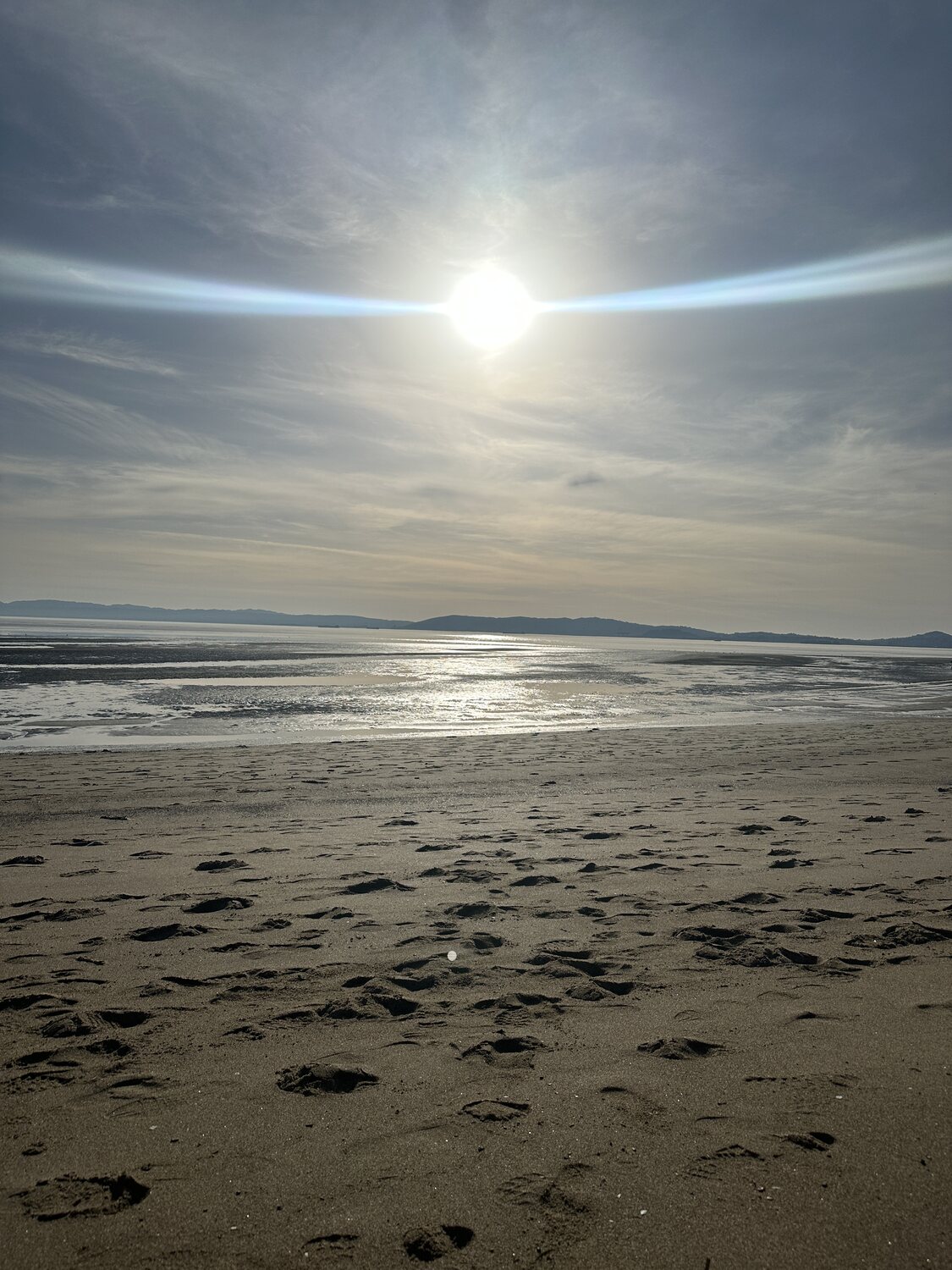 A sun halo over an empty tidal flat, footprints scattered across wet sand