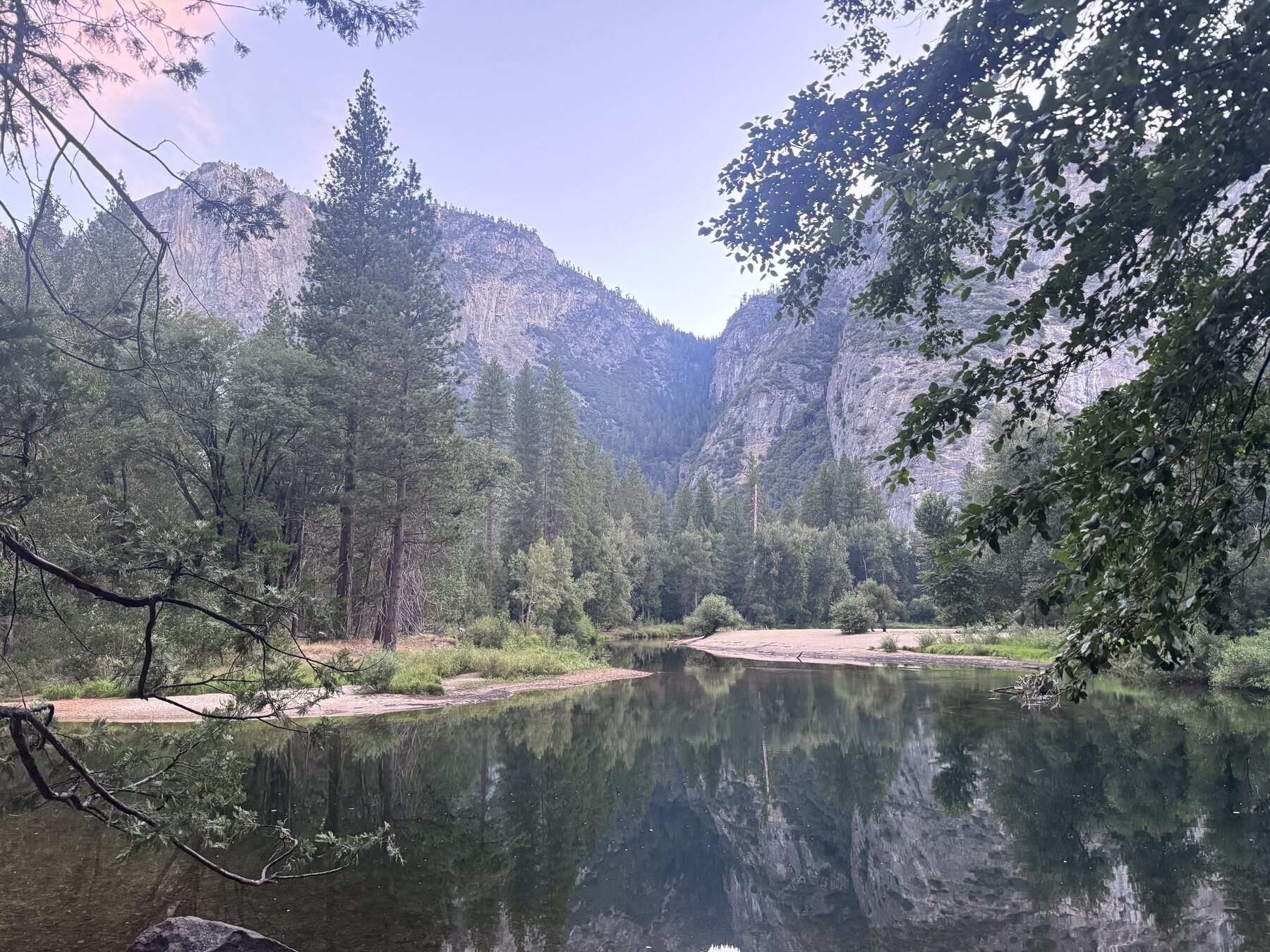 A still river in Yosemite Valley at dusk, granite cliffs and pines mirrored in the water